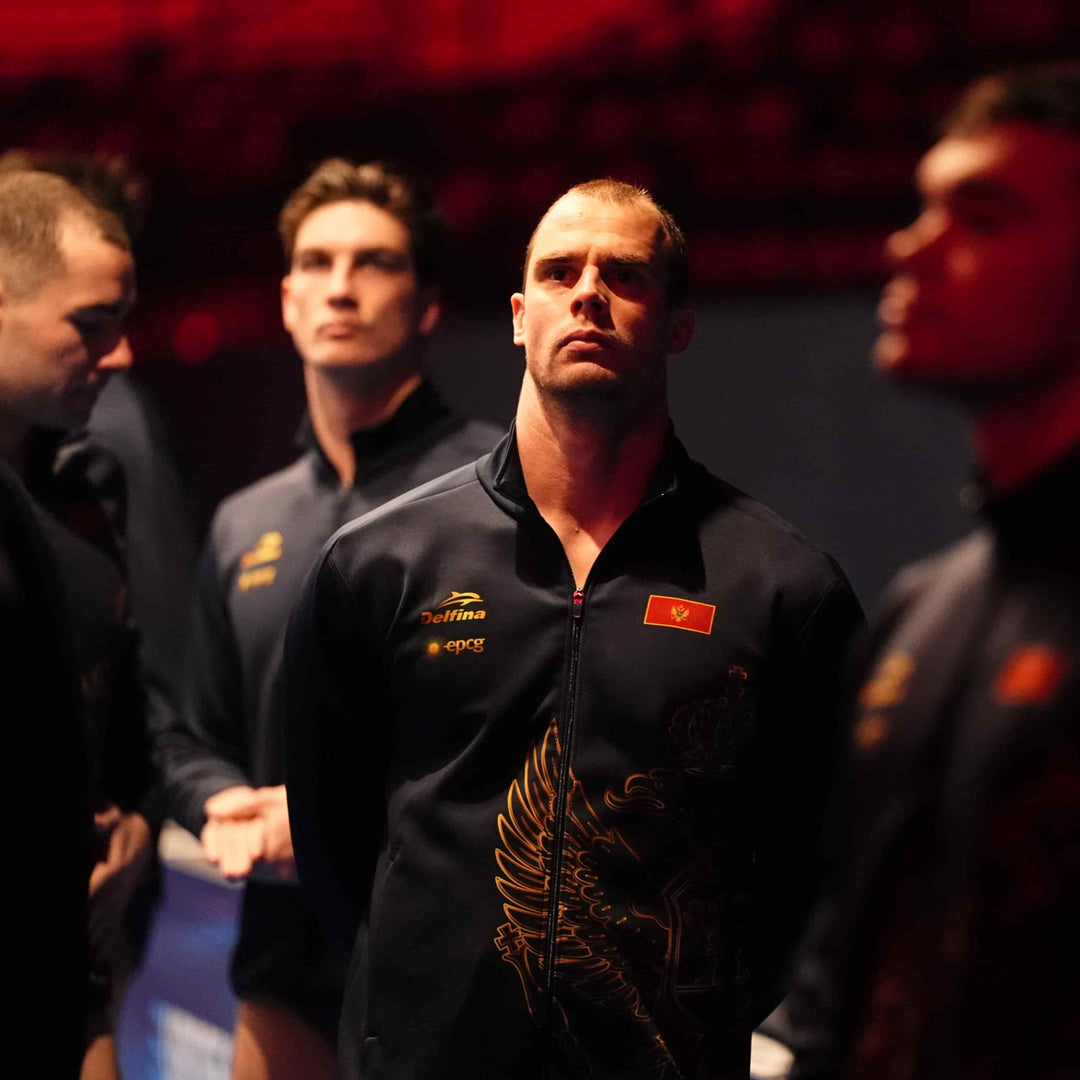 Four men in dark athletic wear standing close together with a red background